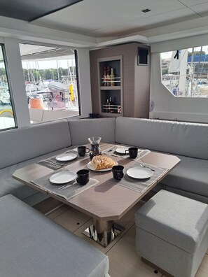 A modern dining area with a central table, cushioned seating, and a view of boats through large windows. - Sun-Kissed Sailing Adventure in Zadar, Croatia (Bibinje)