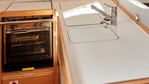 Een compacte keuken met een ingebouwde oven, een spoelbak en een raam boven de spoelbak.