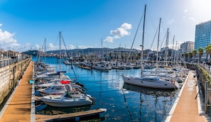 A marina with boats docked along a wooden walkway, surrounded by buildings and a clear sky.
