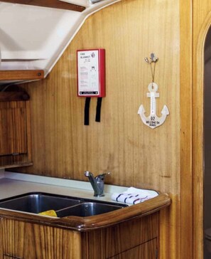 A wooden interior with a kitchen area, including a sink and a fire blanket mounted on the wall. - Sun-kissed Sailing Adventure in the Ionian Islands (Preveza)