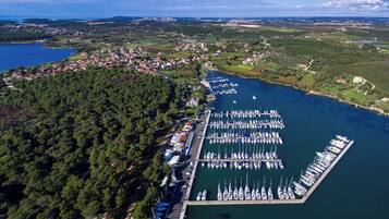 Eine Vogelperspektive eines Yachthafens mit zahlreichen angestaubten Booten, umgeben von einem bewaldeten Gebiet und einer kleinen Stadt im Hintergrund.