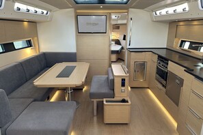Een ruimtelijk ingericht interieur met een bank, tafel, kitchenette en een televisiescherm.