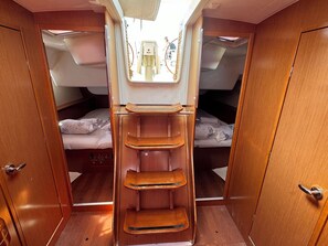 Cabine compacta com duas beliches, uma estante central e uma pequena janela.