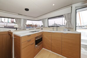 A compact kitchen with wooden cabinets, a built-in oven, a sink, and a window with curtains. - Sun-kissed Sailing Adventure in Split-Dalmatia, Croatia (Trogir)