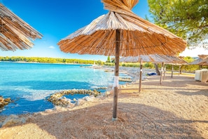 Une plage bordée de parasols en chaume, avec une eau d’un bleu limpide et un rivage rocheux.