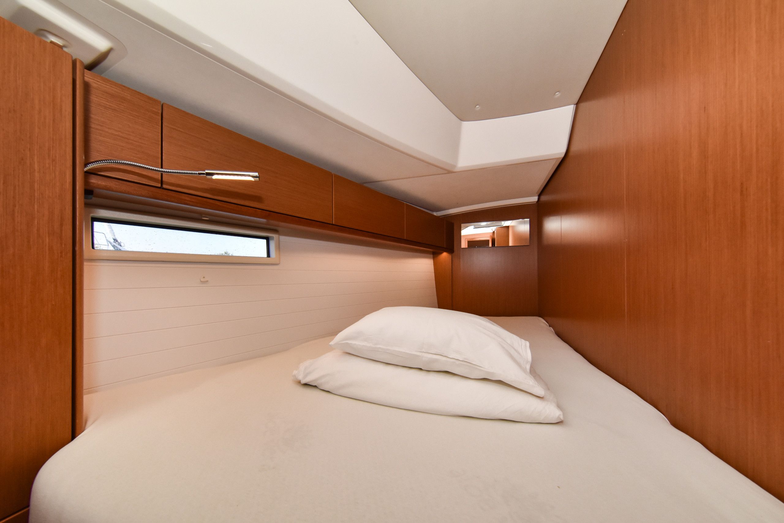 A compact bedroom with a bunk bed, a window, and built-in wooden cabinets.