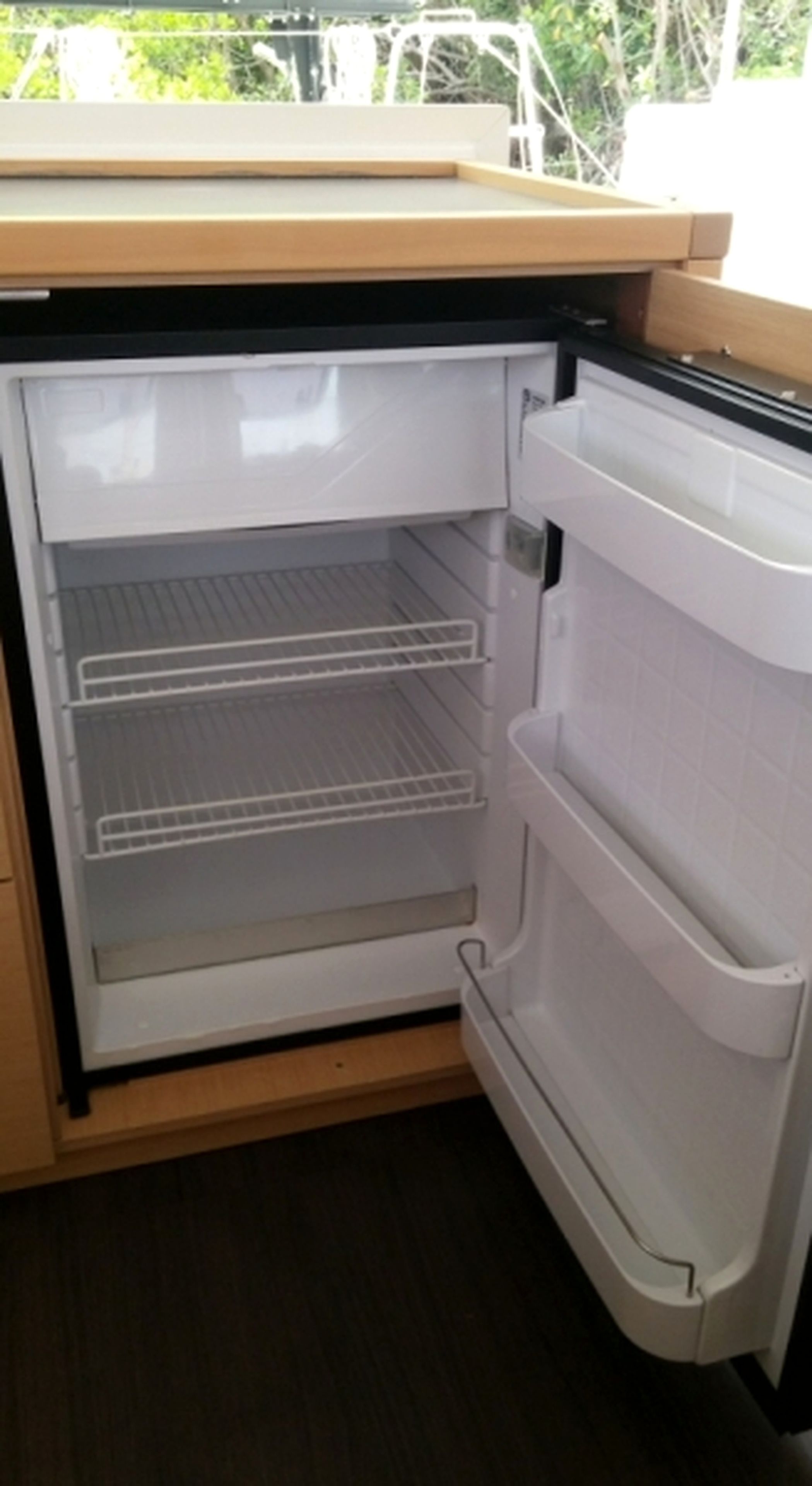Cuina amb nevera integrada, taulell de fusta i finestra amb vista a vegetació.
