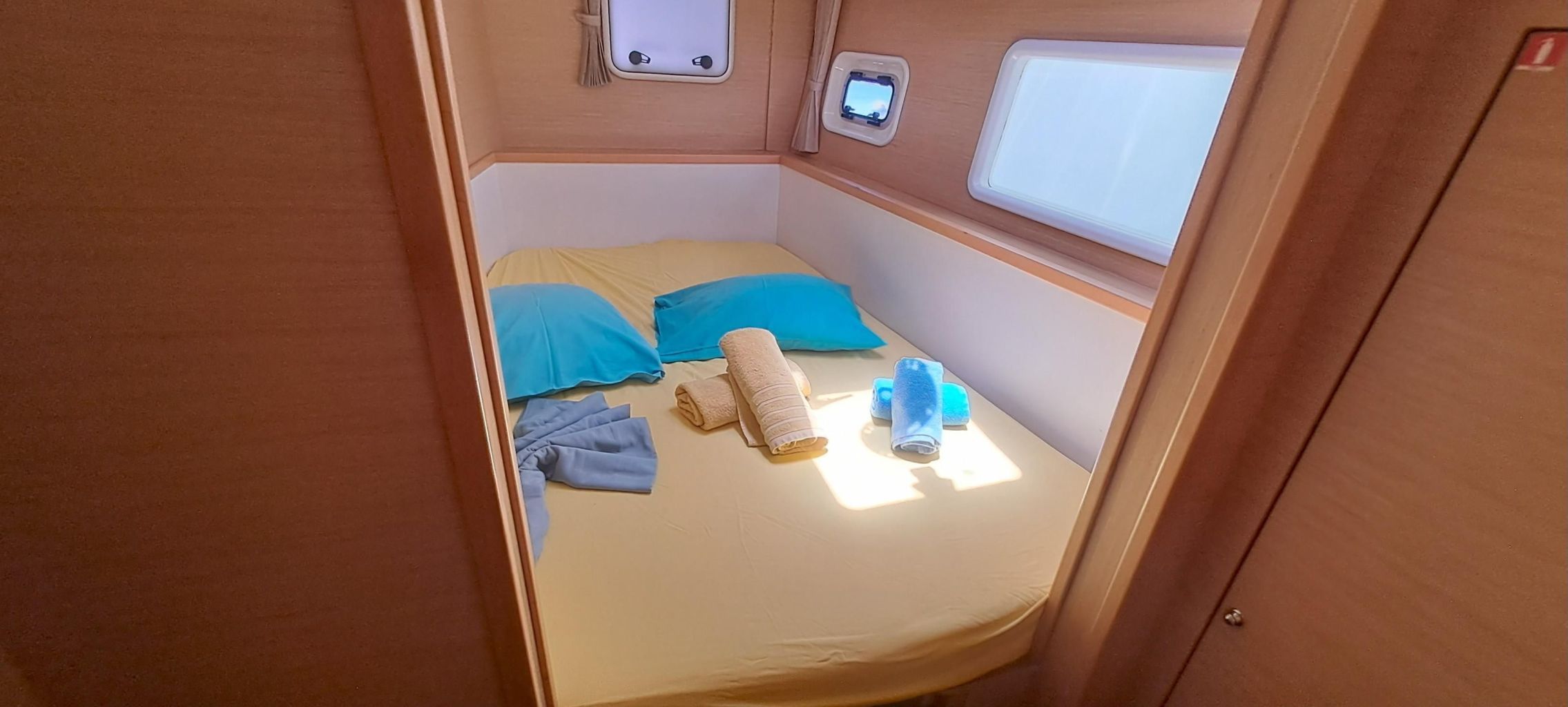 A small, cozy sleeping area with a bed, pillows, a rolled-up towel, and a small window.