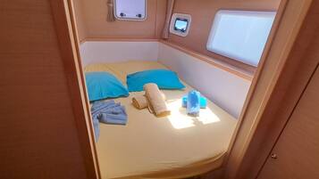 A small, cozy sleeping area with a bed, pillows, a rolled-up towel, and a small window.