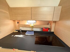 A compact kitchen with wooden cabinets, a black countertop, a built-in stove, and a small vase with flowers. - Sun-Kissed Sailing Adventure in Zadar, Croatia (Biograd na moru)