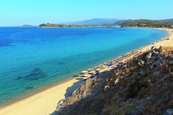 A coastal beach with clear blue water, sandy shore, and rocky terrain.