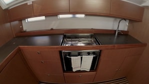 Een praktische keuken met een fornuis, spoelbak en oven, met houten kastjes en een raam boven de spoelbak.