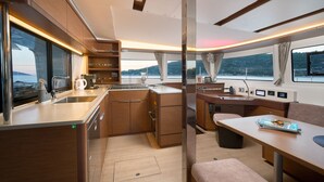 A modern kitchen with a large window, a dining area with a table and bench, and a view of the water outside. - Sun-kissed Sailing Adventure in Split-Dalmatia, Croatia (Trogir)