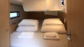 Um quarto compacto e bem iluminado, com uma cama de solteiro, almofadas e toalhas dobradas com cuidado.