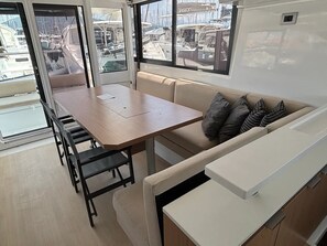 A compact interior with a dining area, a sofa, and a window offering a marina view. - Sun-Kissed Sailing Adventure in the Ionian Islands, Lefkada (Lefkada)