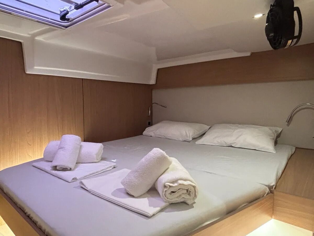 A hotel room with a bed, white linens, a headboard, a window, and a bag hanging on the wall.
