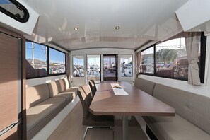 A boat interior with a dining table, cushioned seating, and large windows offering views of the marina. - Sun-kissed Sailing Adventure in Split-Dalmatia, Croatia (Trogir)