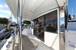 A boat's deck with a glass door, a cushioned seating area, and a flag. - Sun-kissed Sailing Adventure in Split-Dalmatia, Croatia (Trogir)