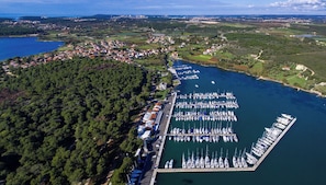 Eine Vogelperspektive eines Yachthafens mit zahlreichen angestaubten Booten, umgeben von einem bewaldeten Gebiet und einer kleinen Stadt im Hintergrund.