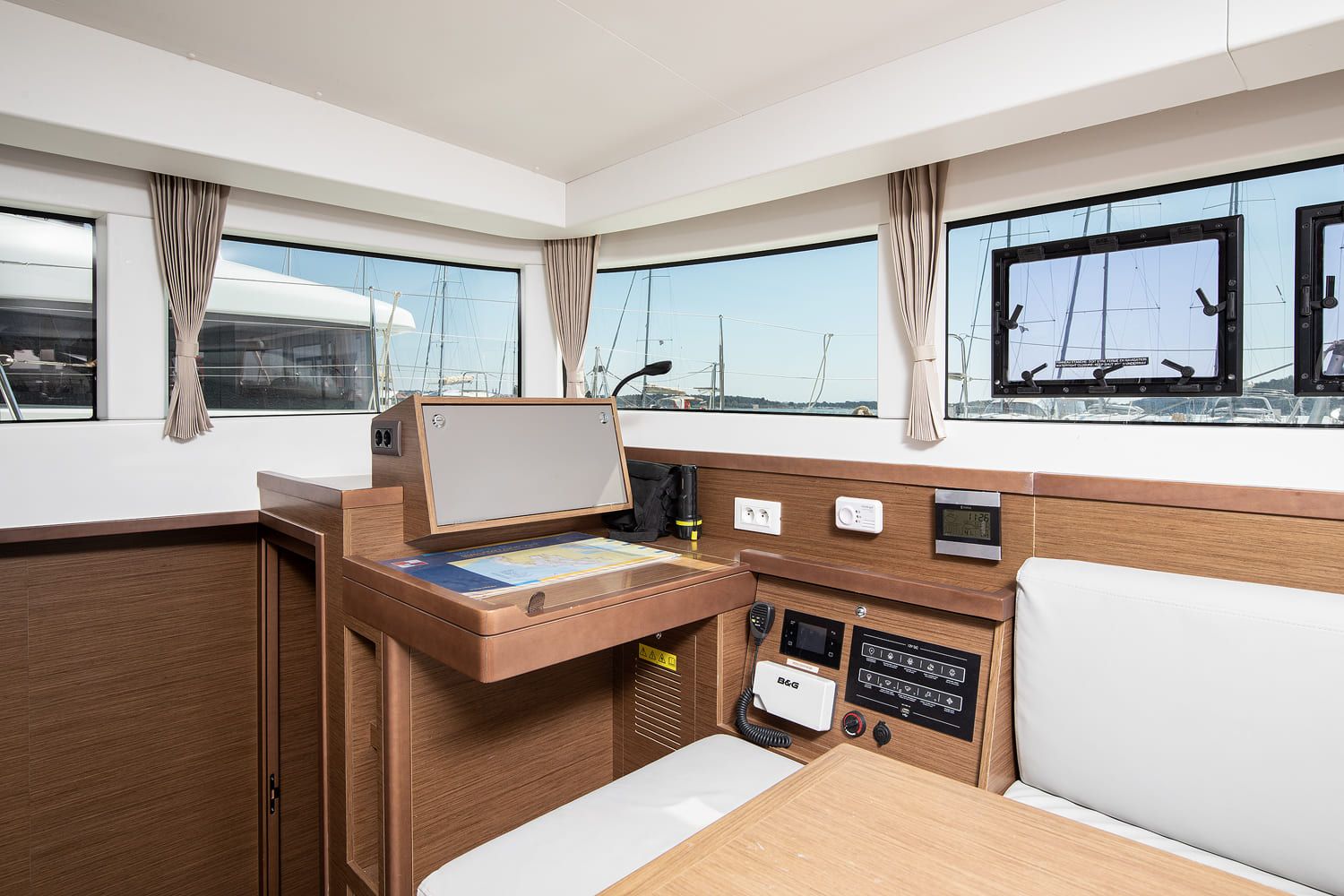 A boat's cabin with a control panel, a map, and windows with curtains.