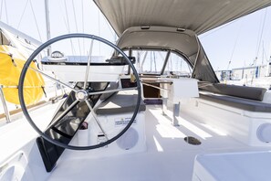A sailboat's interior with a steering wheel, a cushioned seating area, and a small table. - Sun-Kissed Sailing Adventure in Zadar, Croatia (Biograd na moru)