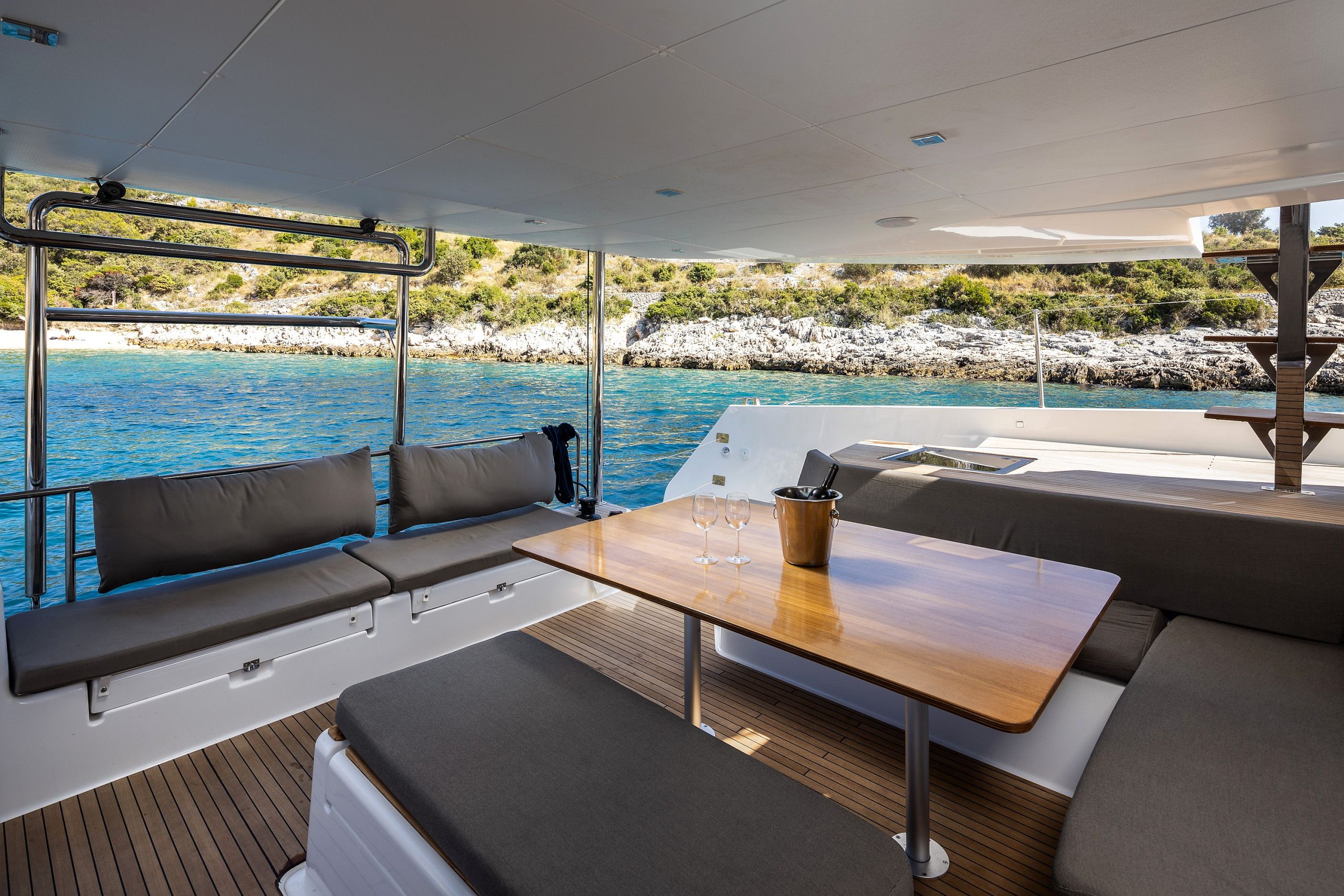 A boat deck with seating, a table, and a view of the sea and rocky coastline.
