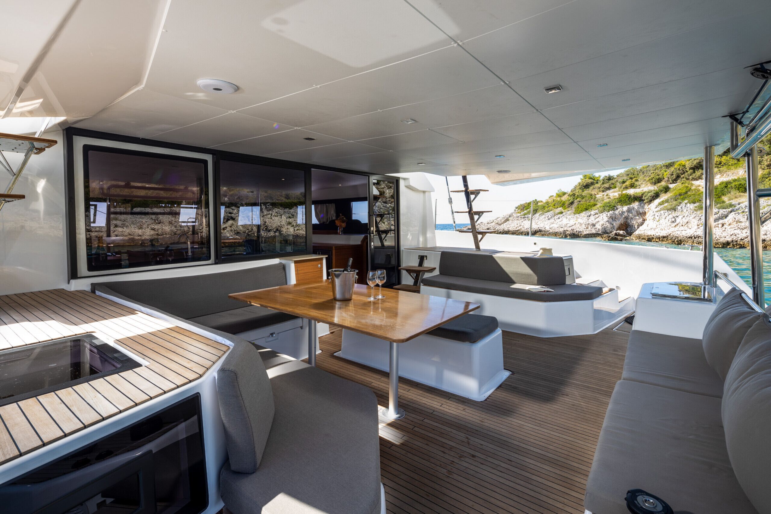 A modern boat interior with a dining area, seating, and large windows offering views of the coastline.