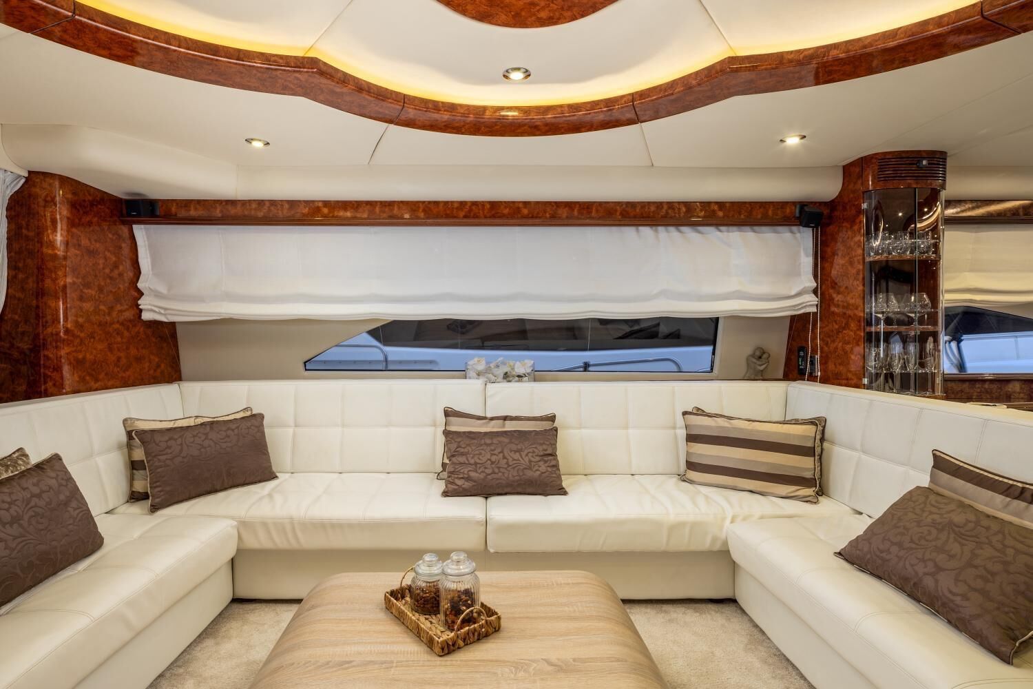 A luxurious cabin with a white upholstered sofa set, a wooden accent wall, and a glass cabinet with glasses.