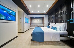 Ein modernes Hotelzimmer mit einem großen Bett, einem Fernseher, einer Sitzecke und Meerblick.