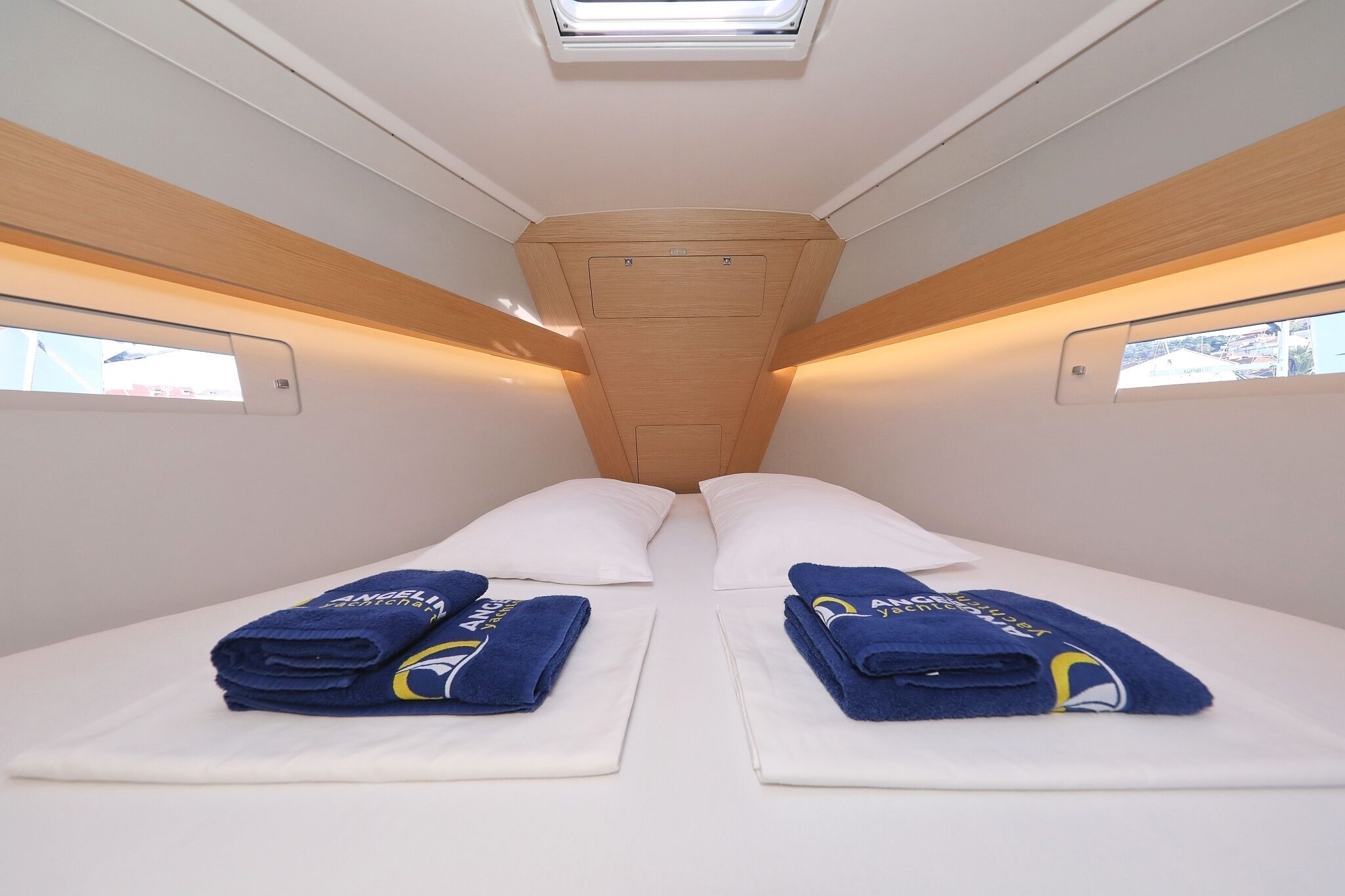 A narrow train compartment with two beds, each with a folded blue towel and a pillow.