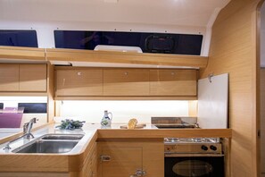 A compact kitchen with wooden cabinets, a sink, a stove, and a small countertop area. - Sun-Kissed Sailing Adventure in Istria, Croatia (Pula)