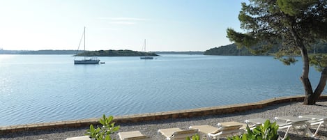 A calm lake with boats, a pebble beach, and lounge chairs.