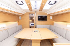 A compact interior with a central table, cushioned seating, a mounted TV, and a skylight. - Sun-Kissed Sailing Adventure in Sibenik, Croatia (Primošten)
