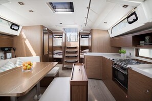A compact kitchen with a stove, sink, and storage cabinets. There is a dining area with a table and bench, and a small seating area with cushions. - Sun-kissed Sailing Adventure in Istria, Croatia (Pomer)