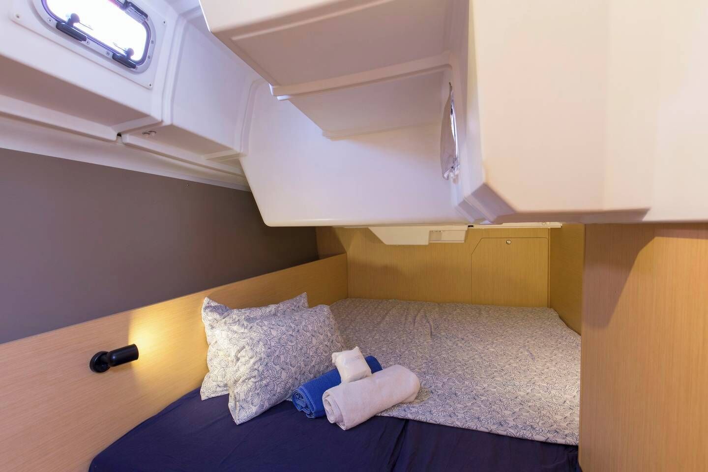 A compact bed with a headboard, a small window, and a storage compartment above.