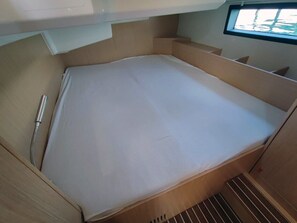 A compact, single-bed RV with a white mattress, a metal shower hose, and a window providing a view of the outdoors. - Sun-Kissed Sailing Adventure in Northern Croatia (Punat)