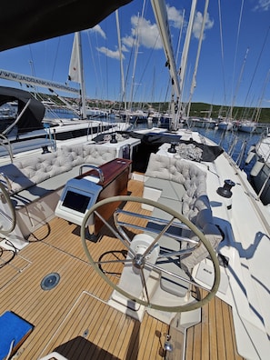 Ein Yachtdeck mit Steuerpult, gepolsterten Sitzgelegenheiten und Bedienfeld.