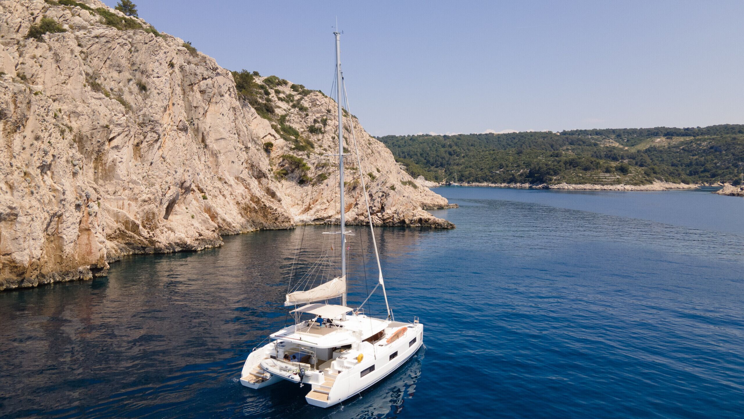 A sailboat anchored near a rocky coastline.