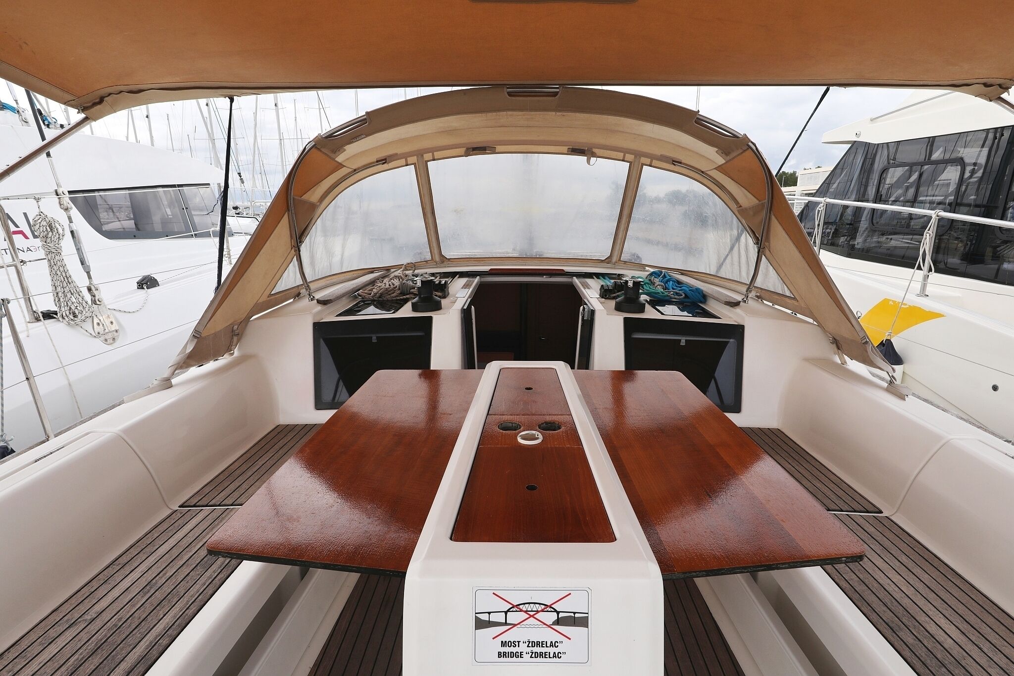 Dek van een boot met een houten tafel, een stuurwiel en een boogbrug met de tekst 'Most 'Zdelac' Bridge 'Zdelac''.