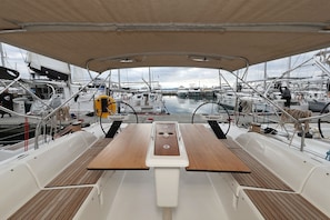 Ein Bootsdeck mit einem zentralen Tisch, hölzernen Bänken und Blick auf andere Boote im Yachthafen.
