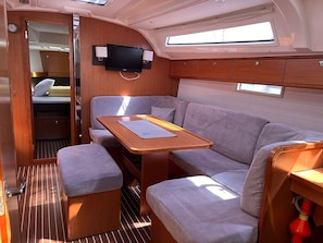 Ein gemütlicher Innenraum mit Sofa, kleinem Tisch, Wandfernseher und Fenster für natürliches Licht.