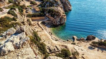 Un site archéologique situé sur la côte, comprenant des ruines, une plage et un terrain rocheux.
