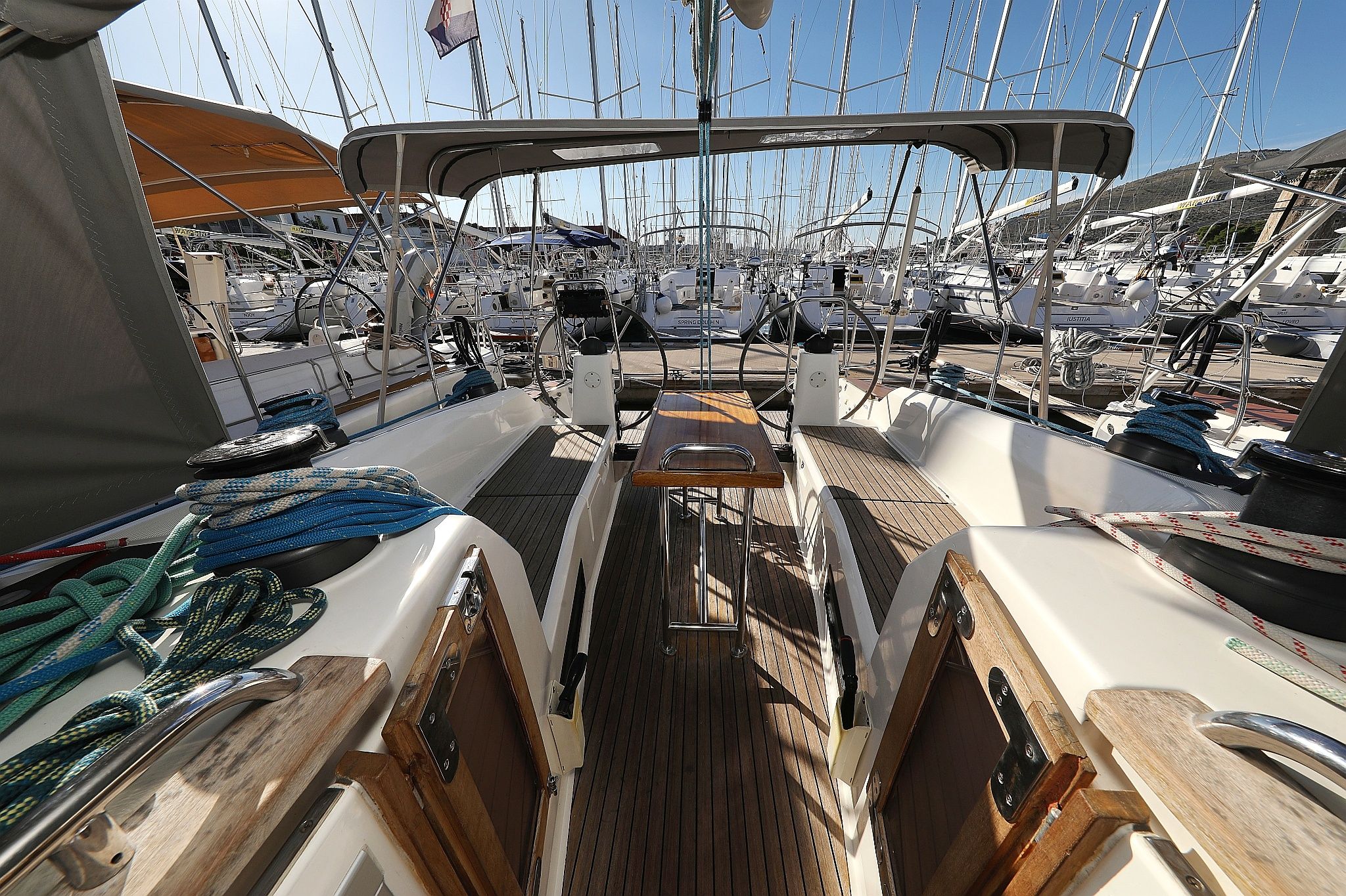 A marina with multiple sailboats docked, wooden deck, and a clear sky.