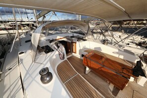 Een scheepdek met een stuurwiel, een roerstand en een houten bank.