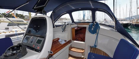 Interior de un barco con timón, panel de control y zona de estar.