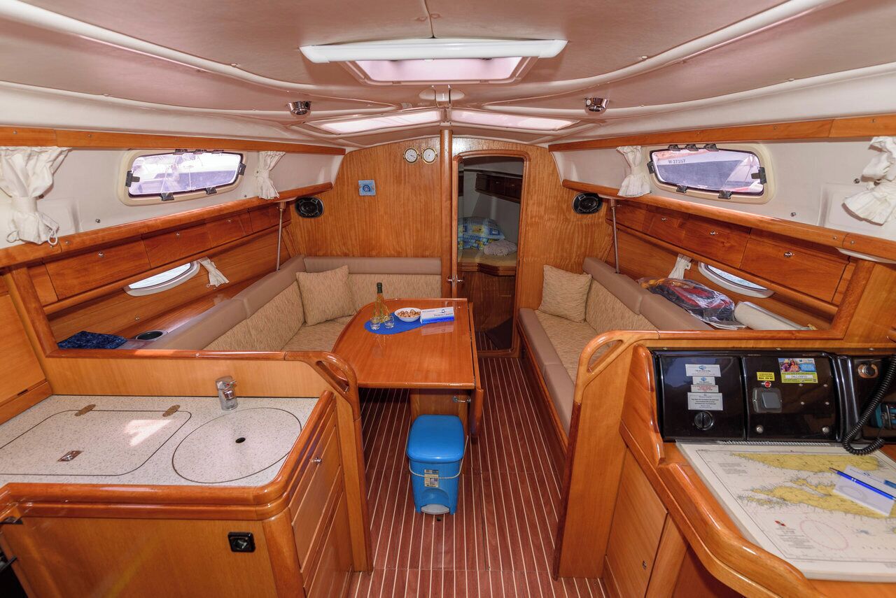A compact boat interior with a central seating area, two windows, a small table, and a control panel.