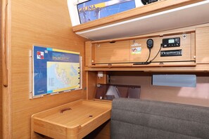 Ein kompaktes Wohnmobil-Interieur mit einer Karte an der Wand, einem kleinen Tisch, einer gepolsterten Sitzgelegenheit und einem Regal mit Radio und Telefon.
