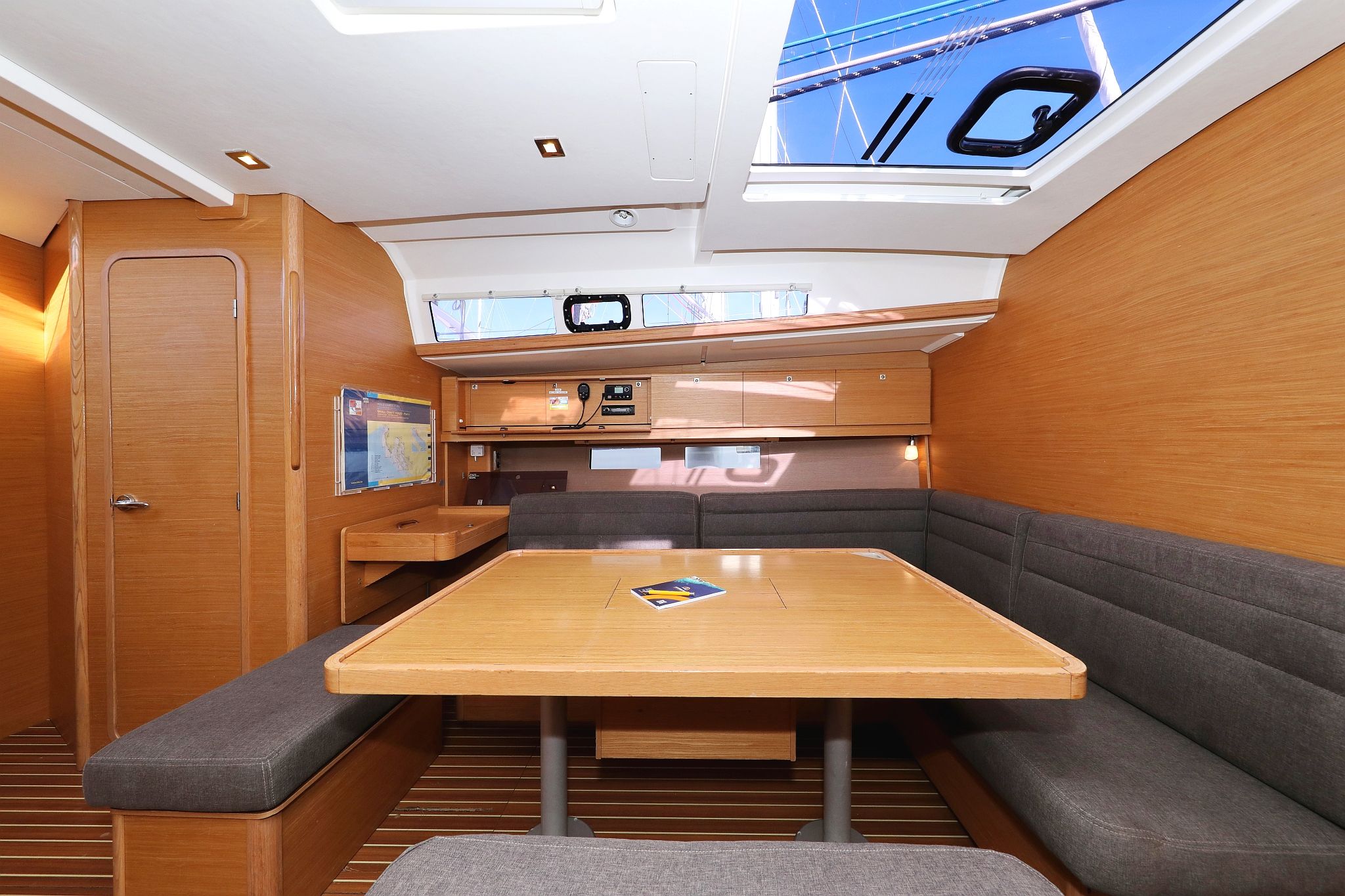 A compact interior with a wooden table, cushioned seating, a small kitchenette, and a skylight.
