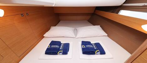 A compact cabin with a single bed, two pillows, and two towels with a logo.