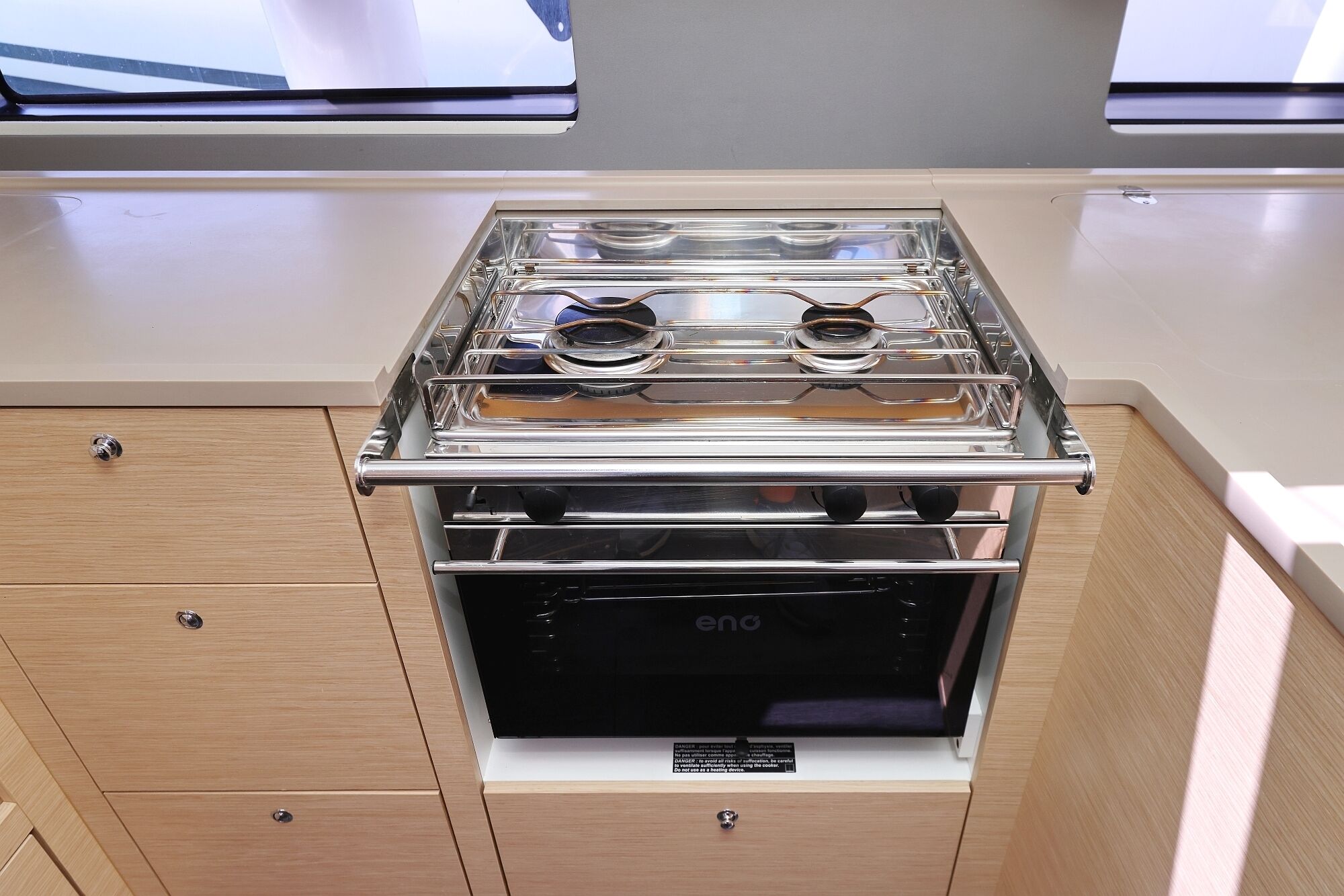 A compact kitchen with a built-in stove and oven, wooden cabinetry, and a window above the stove.
